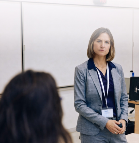 Three professionals in a modern office engage in a focused discussion seated at a table with documents and a laptop. The atmosphere is collaborative.